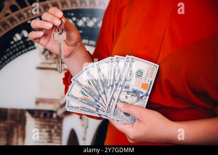 Una ragazza con una camicetta rossa tiene in mano un fan dei dollari americani e le chiavi dell'appartamento. Foto Stock