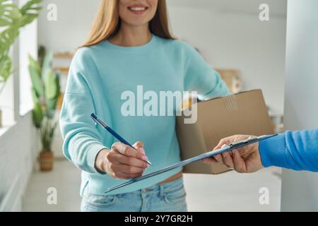 Primo piano di una giovane donna felice che accetta la scatola dal fattorino e firma della carta Foto Stock