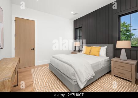 Camera moderna con letto grigio, cuscini gialli, mobili in legno e pareti con accenti neri e finestre. Foto Stock