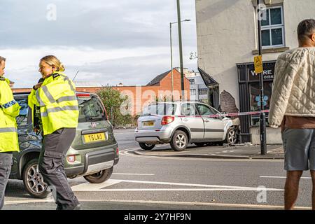 Vista laterale di una piccola auto che si è schiantata all'ingresso di un negozio di fiori, l'auto è circondata da un nastro adesivo, fuoco non incrociare. Agenti di polizia Foto Stock