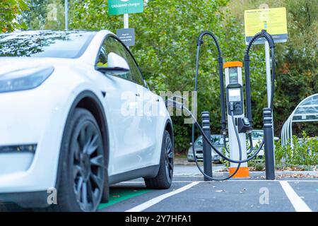 Primo piano di un'auto elettrica bianca che viene caricata presso un punto di ricarica pubblico CHAdeMO EV in un supermercato Sainsbury del Regno Unito. Foto Stock