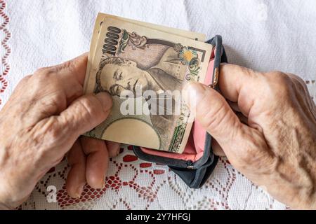 La nonna ha in mano una borsa vecchio stile con yen giapponesi. Concetto, la situazione dei pensionati in Giappone. primo piano Foto Stock