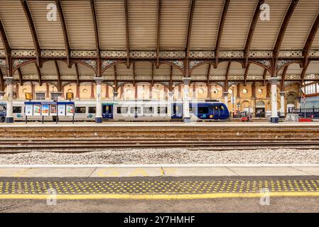 Uno storico arco curvo copre la piattaforma della stazione ferroviaria e un treno aspetta di partire. Un bordo piattaforma con pavimentazione tattile è nel foregro Foto Stock