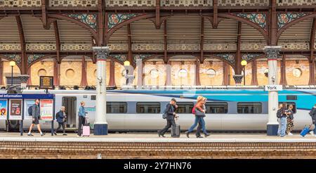 Un treno moderno si trova in una storica piattaforma della stazione ferroviaria sotto una tettoia di ferro del XIX secolo. Una bacheca e le schermate di partenza sono sulla piattaforma Foto Stock