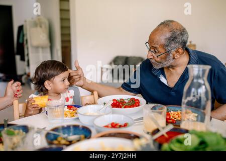 Nonno che parla con la nipote seduta a tavola durante il pranzo a casa Foto Stock