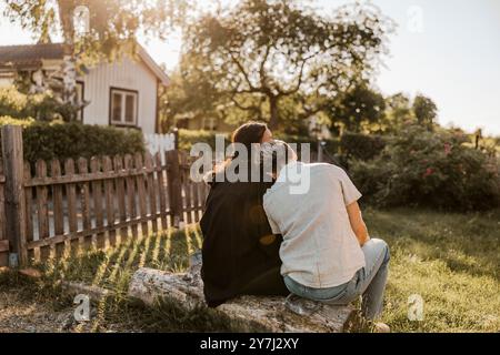 Vista posteriore di una giovane donna seduta con la testa sulla spalla di un'amica nel cortile posteriore Foto Stock
