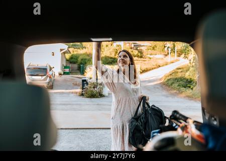 Donna matura che tiene in mano la borsa e chiude il bagagliaio mentre si trova sul vialetto Foto Stock