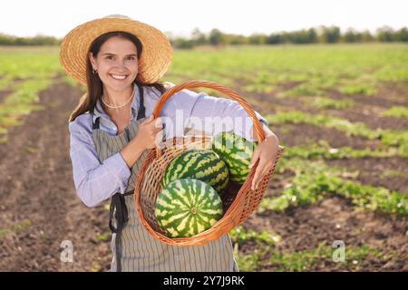 Donna che tiene in mano un cesto di vimini con anguria matura sul campo Foto Stock