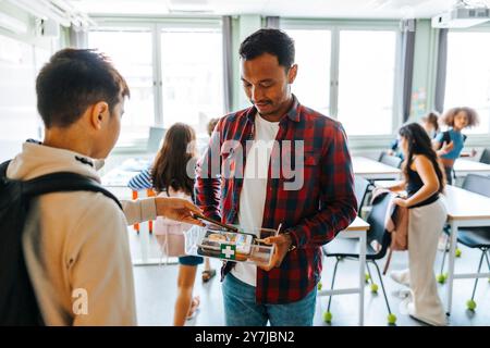 Professore di sesso maschile che raccoglie smartphone di studenti mentre si trova in classe alla scuola elementare Foto Stock