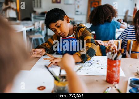 Ragazzo che dipinge le dita su carta durante la lezione d'arte alla scuola elementare Foto Stock