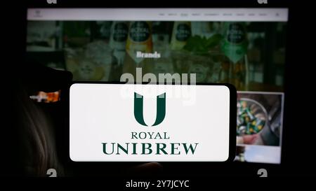 Persona che detiene lo smartphone con il logo della birreria danese Royal Unibrew sullo schermo di fronte al sito Web. Mettere a fuoco il display del telefono. Foto Stock