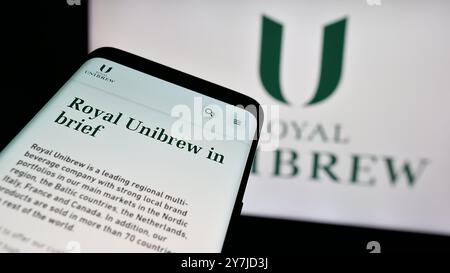 Telefono cellulare con sito Web della birreria danese Royal Unibrew sullo schermo di fronte al logo aziendale. Mettere a fuoco in alto a sinistra sul display del telefono. Foto Stock