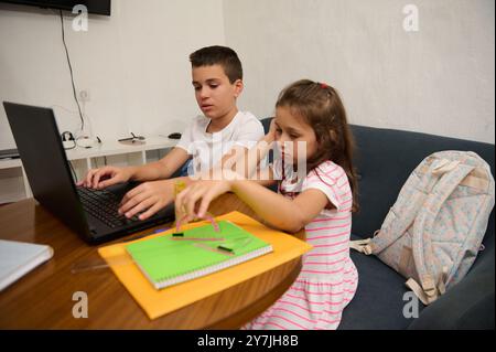 Due bambini si sono concentrati sui compiti con un notebook e un notebook. Un ambiente che riflette l'apprendimento e la concentrazione in un ambiente domestico. Foto Stock