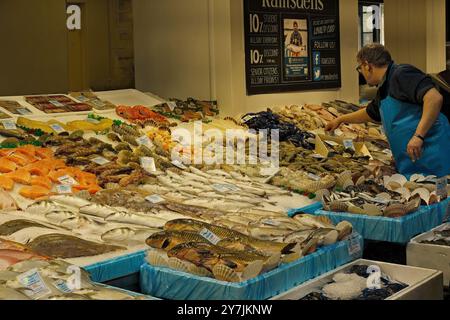 Un uomo rivestito di grembiule lavora attraverso una mostra di pesce fresco e frutti di mare in un mercato di pesce a Leeds, Regno Unito. Foto Stock