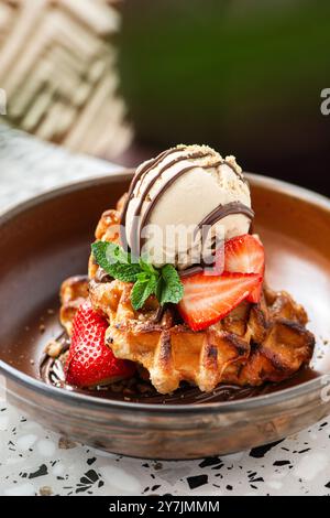 Waffle all'americana con gelato, fragole, sciroppo d'acero e gocce di cioccolato fondente. Foto Stock