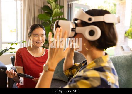 Utilizzando il visore VR, la madre interagisce mentre la ragazza con un tablet sorride nelle vicinanze Foto Stock