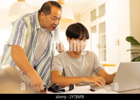 Padre asiatico e figlio adolescente che usano il laptop insieme a casa, concentrandosi sul lavoro Foto Stock Padre asiatico e figlio adolescente che usano il laptop insieme a casa, concentrandosi sul lavoro Foto Stock