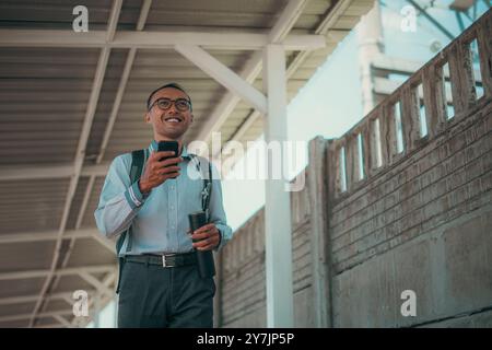 Un giovane uomo sicuro di sé che percorre una città vivace con il suo smartphone Foto Stock