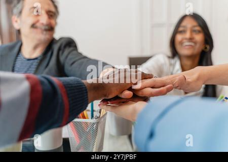 Primo piano di diversi membri del team aziendale che si uniscono per mano in ufficio, simboleggiando l'unità, la cooperazione e l'inclusione sul luogo di lavoro. Multietnico e multigenere Foto Stock