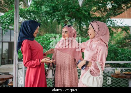 Tre donne vestite di coloratissimi hijab sono impegnate in una conversazione allegra all'aperto Foto Stock