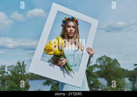 Bella giovane donna Ucraina in corona floreale che regge la cornice con il cielo blu sullo sfondo Foto Stock