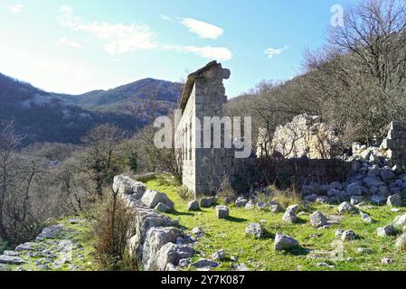 Rovine di una vecchia casa: Un edificio fatto di grandi blocchi di pietra con un muro pesantemente danneggiato e un tetto crollato sullo sfondo delle montagne Foto Stock