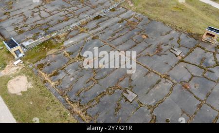 Vista aerea di una superficie in cemento abbandonata con crepe e vegetazione sovrastata. Un tempo era un campo da basket. L'area mostra segni di abbandono, wi Foto Stock