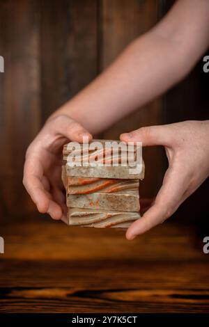 Un paio di mani culla con cura una pila di quattro saponette fatte a mano, ciascuna con un motivo unico e tonalità calde e terrose. Foto Stock