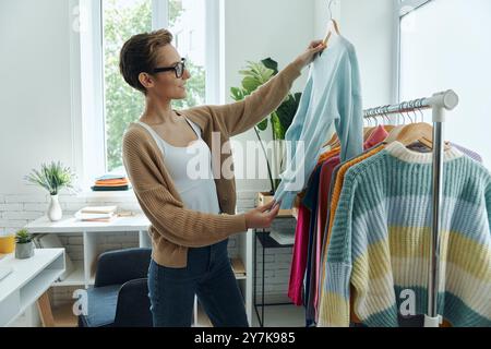Giovane donna sicura di sé che esamina i vestiti mentre lavora in un negozio di moda Foto Stock