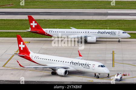 Zurigo, Svizzera, 5 maggio 2024: Un Helvetic Airways Embraer 190LR è gestito da personale di terra. Registrazione HB-JVN. Dietro di esso, un Embraer E190- Foto Stock