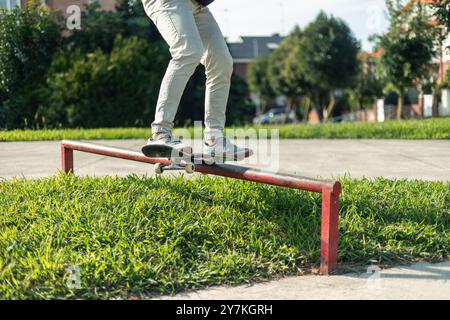 l'immagine ravvicinata ad angolo basso mostra le gambe di uno skater mentre eseguono una macinatura su un'impressionante rotaia rossa nello skate park. enfatizza l'intensità di Foto Stock