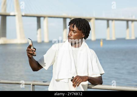 Giovane che scatta un selfie sul lungomare con un ponte sullo sfondo Foto Stock