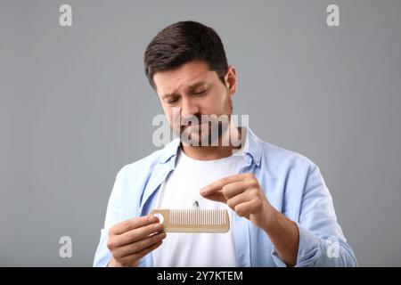 Uomo triste che prende i capelli persi dal pettine su sfondo grigio. Problema di alopecia Foto Stock