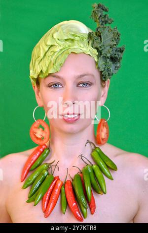 Un ritratto audace e giocoso che combina prodotti freschi, con un look vivace fatto di peperoni, pomodori e verdi frondosi su uno sfondo verde vivace. Foto Stock