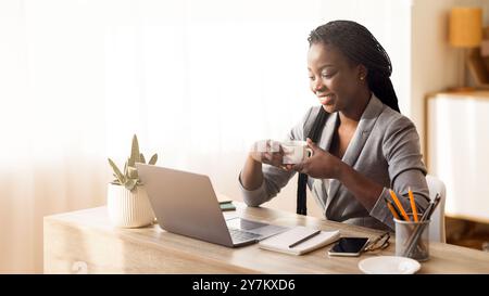 Donna d'affari afro di successo che beve caffè sul posto di lavoro in un ufficio moderno Foto Stock
