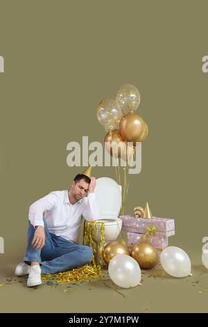 Giovane con sbornia seduto vicino alla ciotola del water dopo la festa di compleanno su sfondo verde Foto Stock