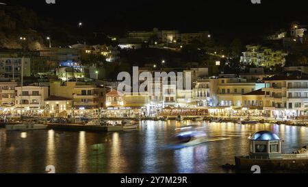 Foto notturna di un porto con edifici illuminati e luci riflettenti nell'acqua, Pigadia, la città e il porto, Pigadia Bay, la città principale, Karpathos, D. Foto Stock