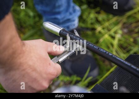 Una persona controlla un cavo nero all'esterno con un calibro, installazione in fibra ottica, distretto di Calw, Foresta Nera, Germania, Europa Foto Stock