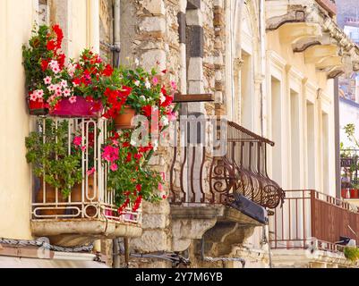 Costruzione di facciate e balconi nelle strade di Taormina piene di fiori di bouganville in una soleggiata giornata estiva, Sicilia, Italia Foto Stock