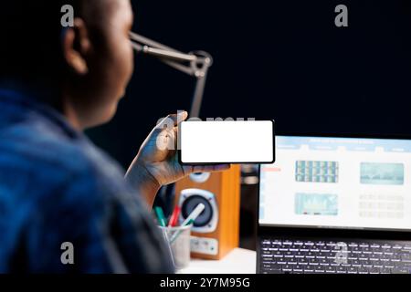 Primo piano di un freelance che lavora da casa, utilizzando un laptop e uno smartphone che visualizza un modello di copia vuoto. Donna nera che guarda uno schermo bianco isolato su un dispositivo mobile. Foto Stock