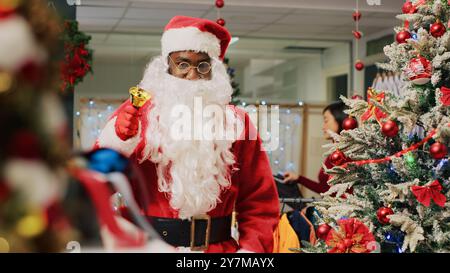 Lavoratore vestito da Babbo Natale che diverte gli amanti dello shopping in occasione delle feste natalizie adornano il negozio di moda durante la stagione invernale. Assistente al dettaglio che condivide lo spirito festivo con i clienti che visitano il negozio di abbigliamento Foto Stock