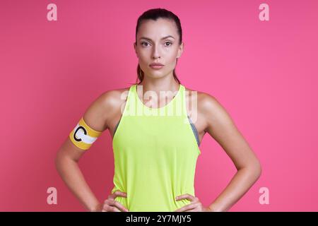 Donna sicura di sé in abbigliamento sportivo con fascia capitano e in piedi su sfondo rosa Foto Stock