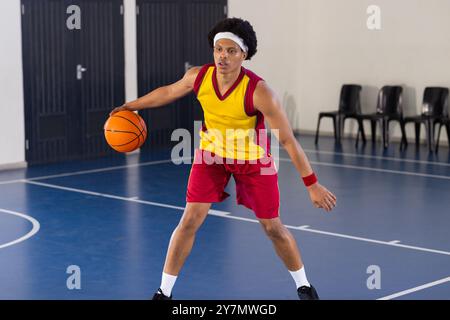 Pallacanestro da dribbling sul campo interno, atleta in uniforme rossa e gialla Foto Stock