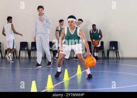 Dribbling di pallacanestro intorno ai coni, giovane atleta che pratica nella palestra scolastica Foto Stock