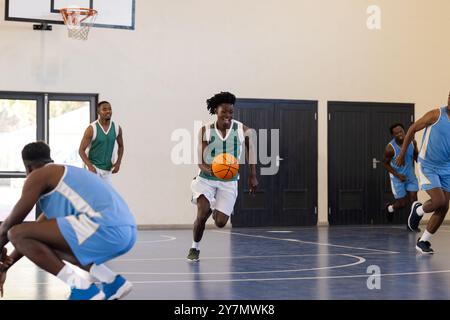 Giocando a basket, uomo che dribbling ball su un campo al coperto con i compagni di squadra Foto Stock