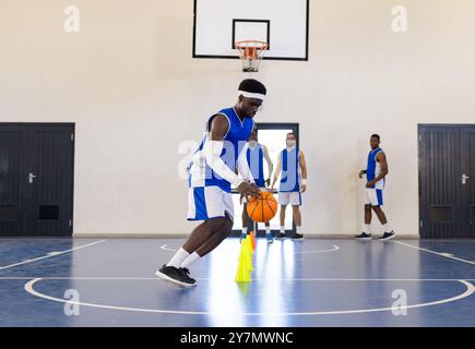 Dribbling di basket intorno ai coni, atleta che pratica abilità sul campo al coperto Foto Stock