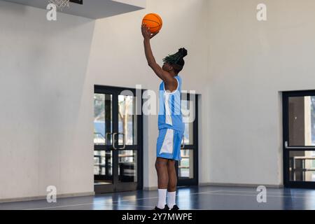 Giocando a basket, atleta con la palla blu uniforme che tira su cerchio all'interno Foto Stock