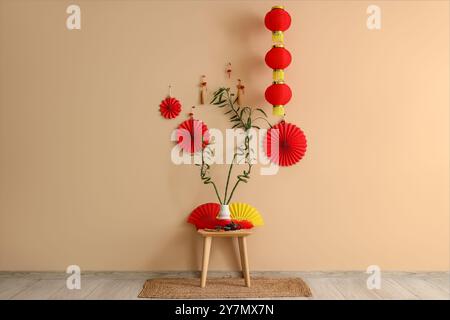 Tavolo con set da tè, steli di bambù e ventilatori di carta vicino alla parete beige. Festa del capodanno cinese Foto Stock