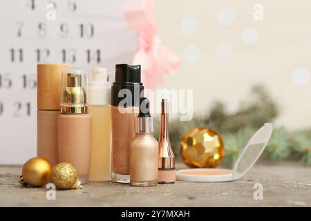 Cosmetici decorativi con palle di Natale sul tavolo contro il calendario dell'Avvento sfocato, primo piano Foto Stock