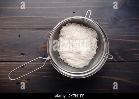 Tagliatelle di riso Vermicelli cotte e sgocciolate: Spaghetti di riso con capelli d'angelo sottili in un filtro a rete posto su un recipiente di miscelazione Foto Stock